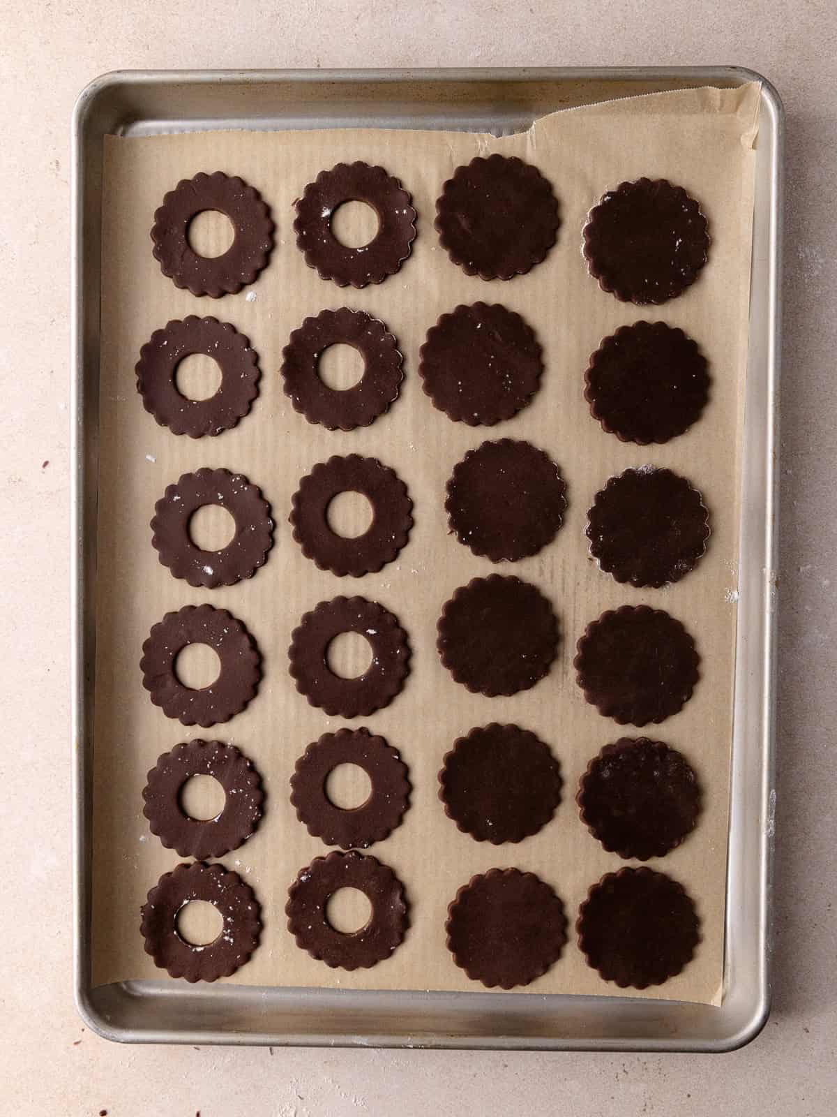 Chocolate linzer cookies are sitting on a large baking sheet.