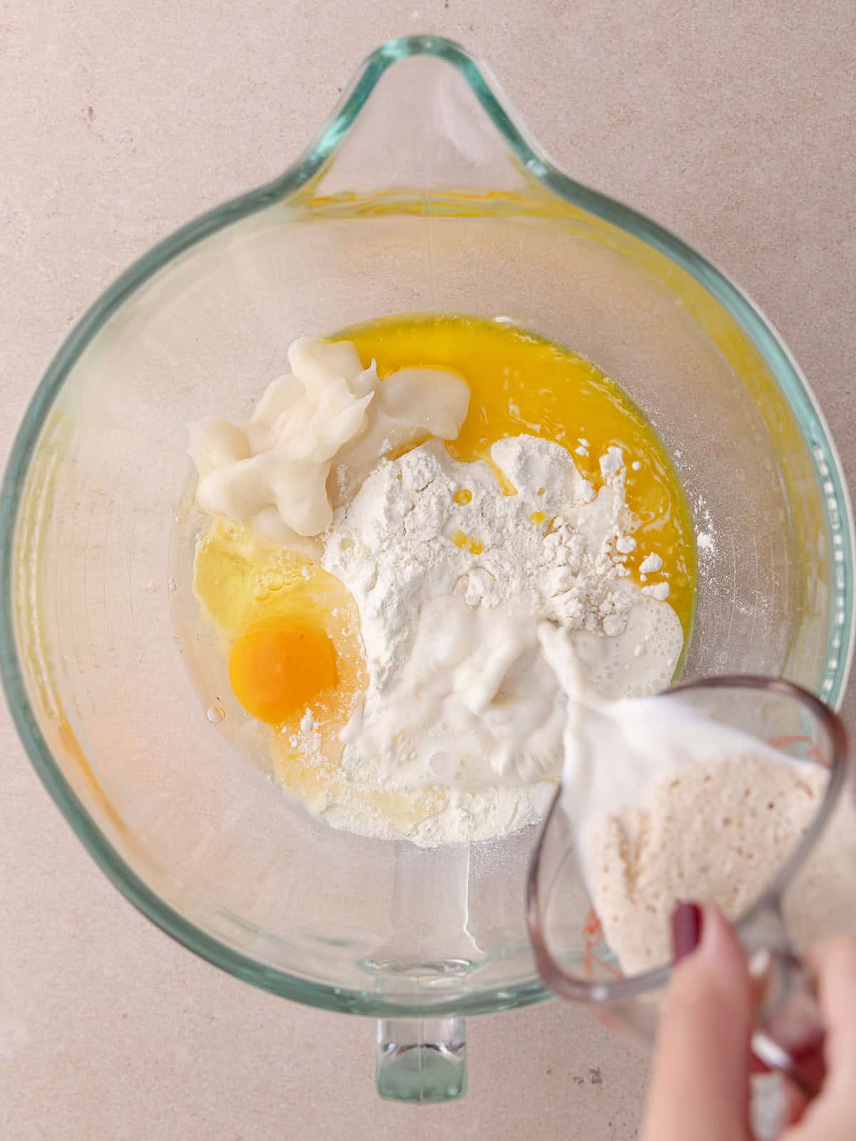 Bloomed yeast mixture is poured into a glass bowl with other Tangzhong wool bread dough ingredients.