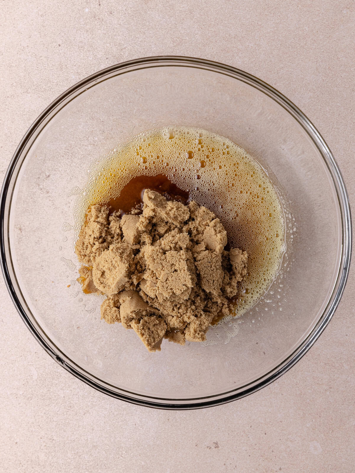 Hot brown butter and brown sugar are added to a large glass mixing bowl.