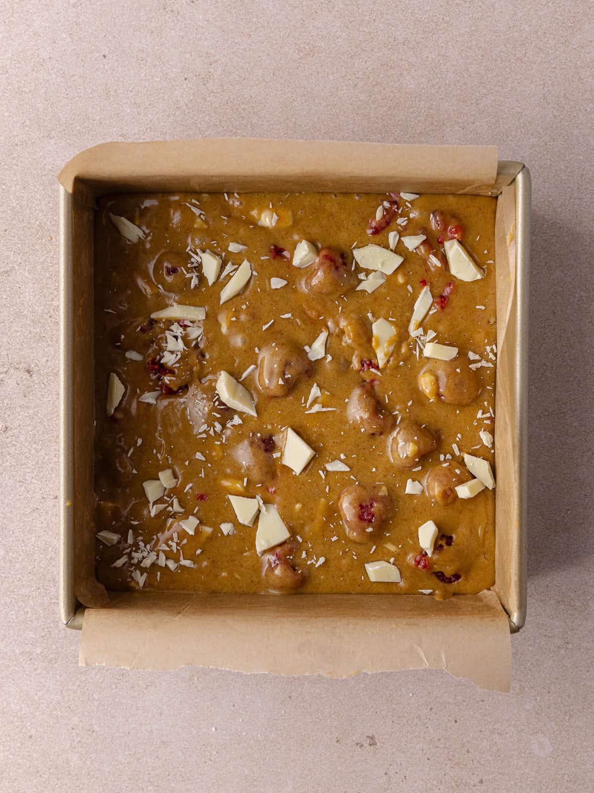 White chocolate raspberry blondies batter is transferred to a small square baking pan.