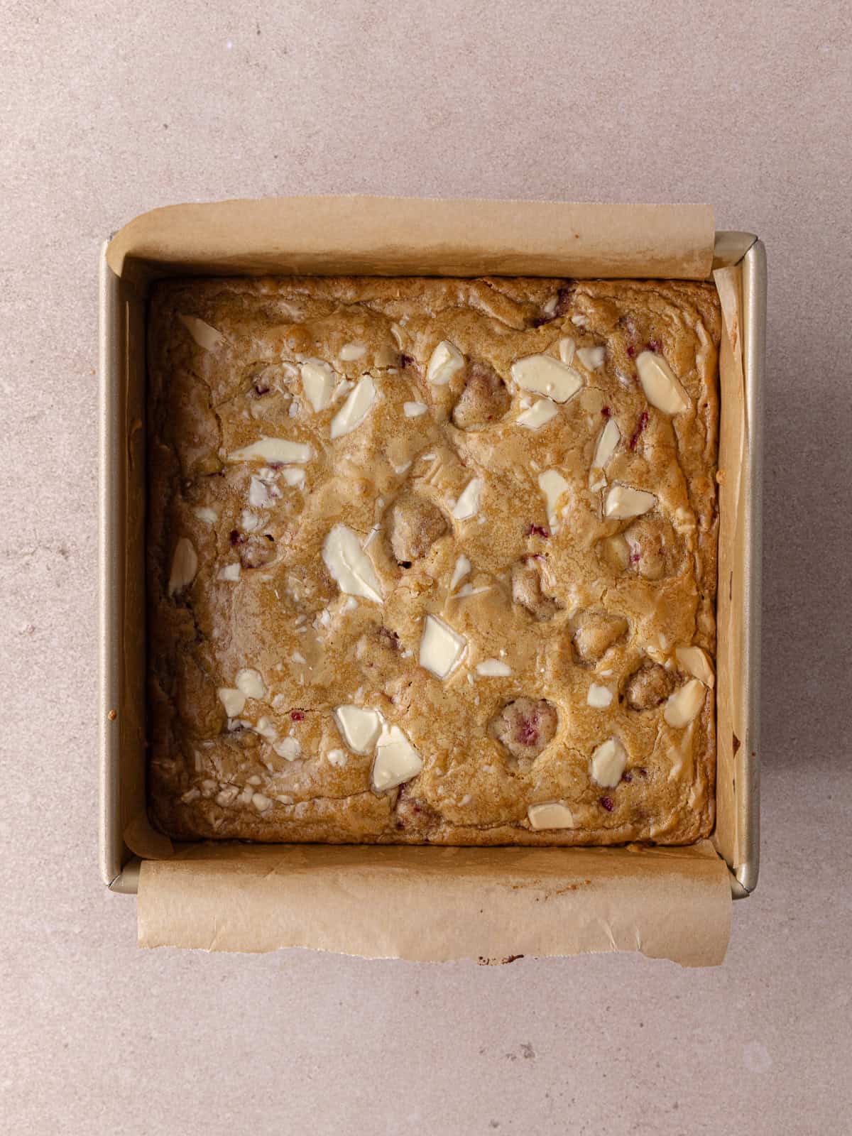 White chocolate raspberry blondies are baked until golden and sitting in a baking pan.