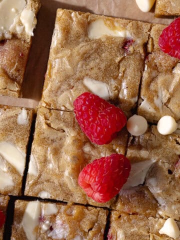 Gooey and fudgy brown butter raspberry and white chocolate blondies are cut into small squares, feature photo.