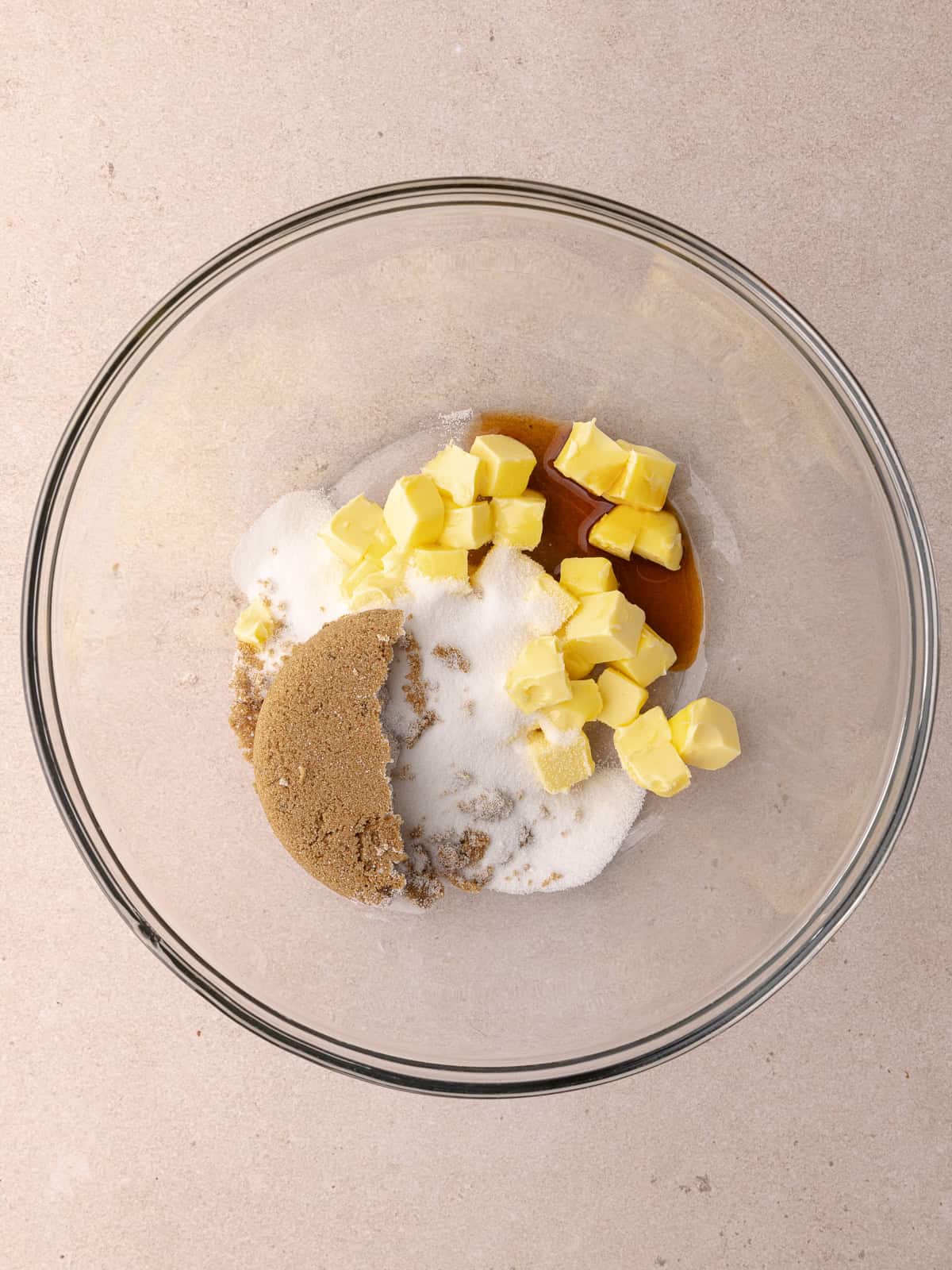 Softened butter, brown sugar, white sugar and vanilla are in a large glass mixing bowl.