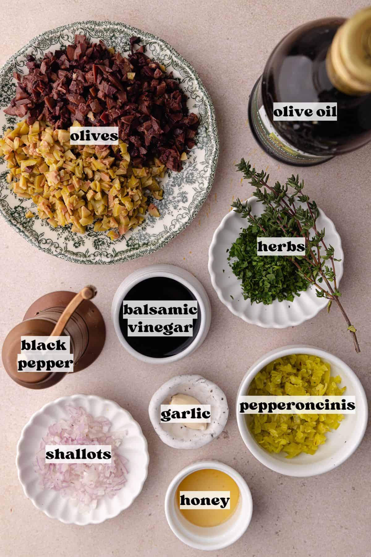 Olive tapenade ingredients which include, green olives, kalamata olives, pepperoncinis, basil, parsley, thyme, honey, extra-virgin olive oil, balsamic vinegar and black pepper.