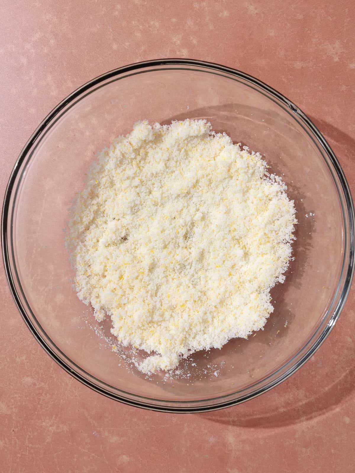 White sugar and lemon zest are rubbed together in a large glass bowl.