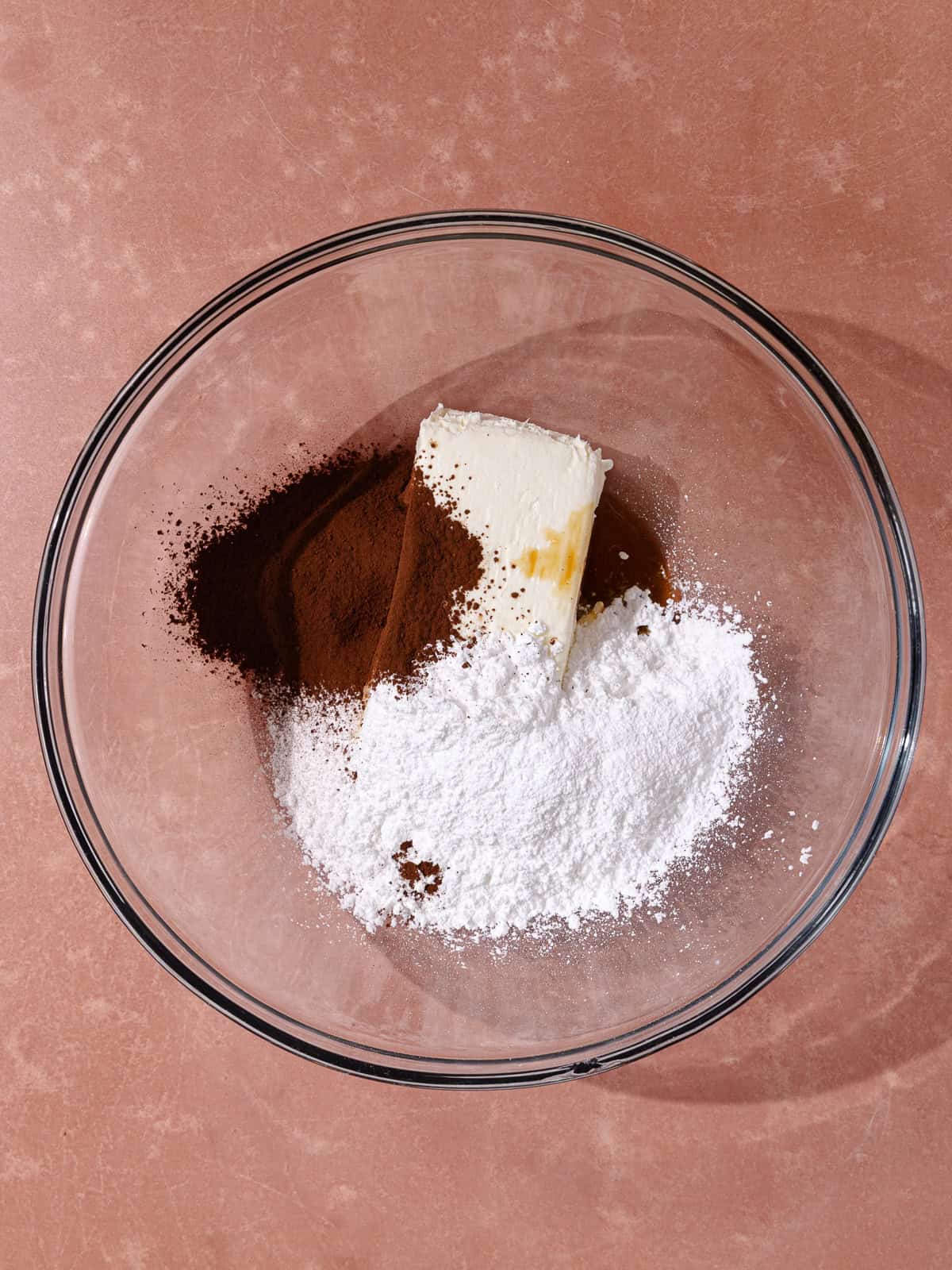 Softened cream cheese, Dutch-process cocoa powder, powdered sugar and vanilla extract are in a large glass bowl.