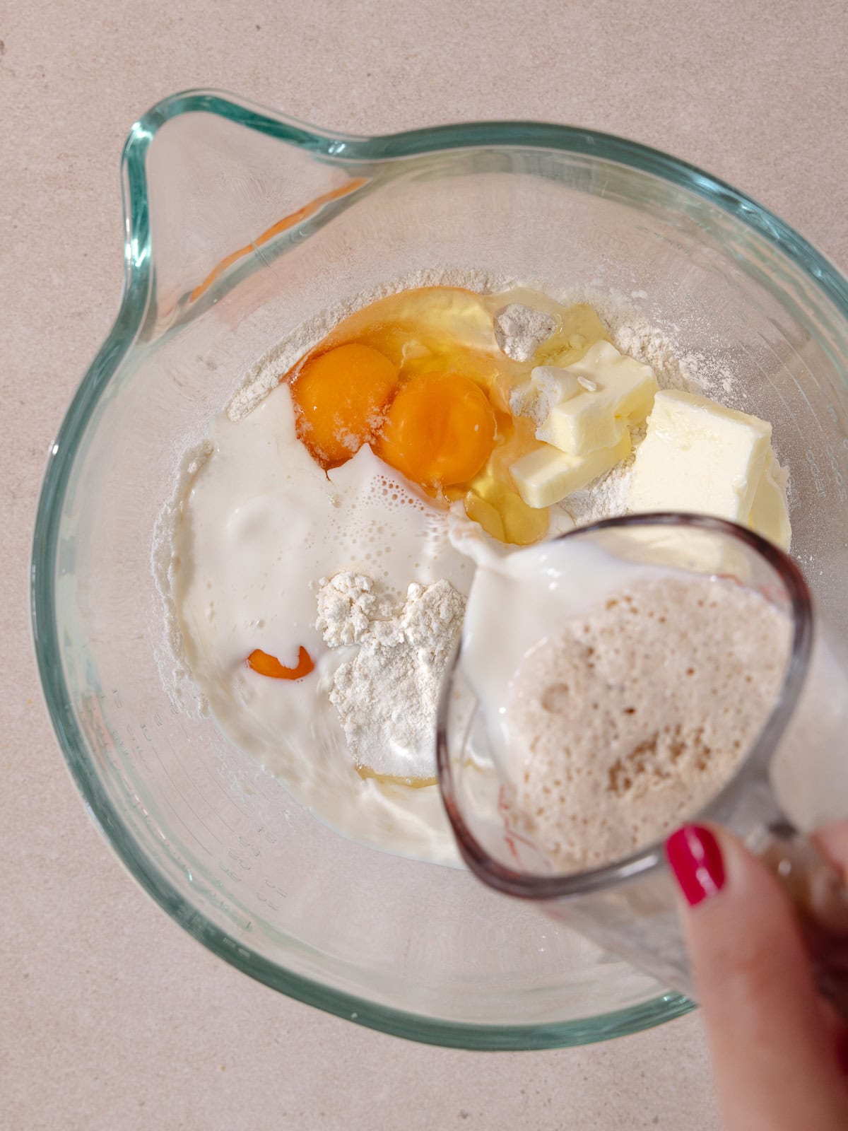 Frothy yeast milk mixture is poured into the stand mixer bowl with all brioche donut ingredients.