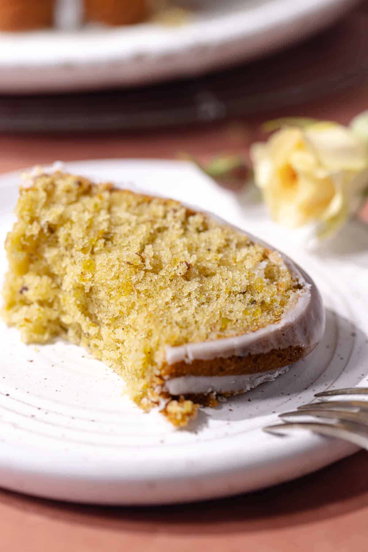 A slice of Pistachio rose cardamom olive oil cake with rose water glaze sitting on a dessert plate.