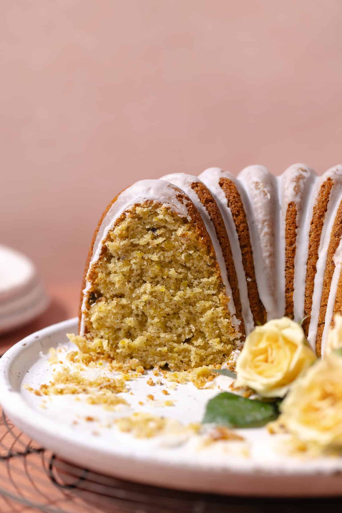 Pistachio rose cardamom olive oil cake with rose water glaze sitting on a serving plate.