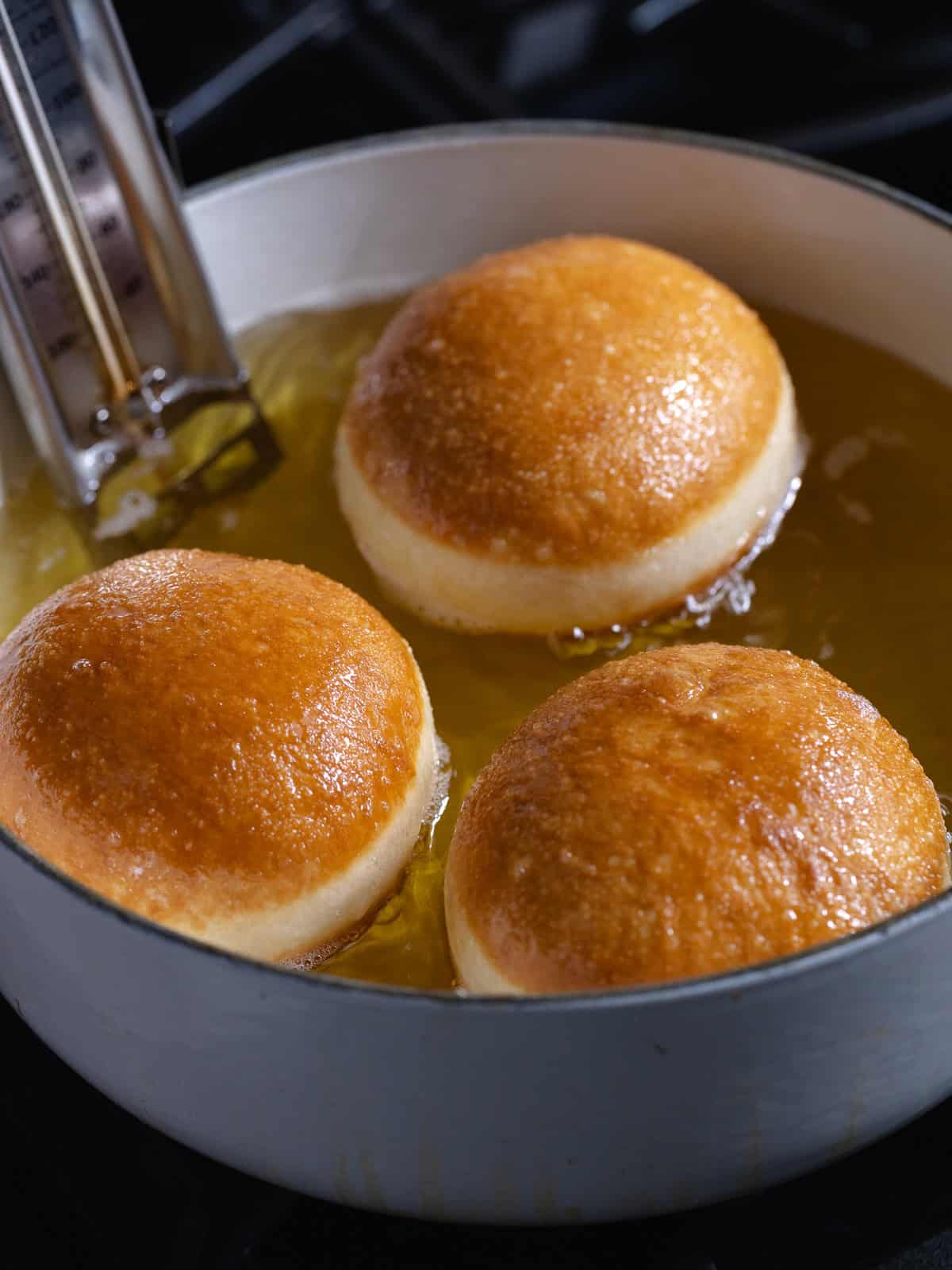 Donuts are deep fried in a white dutch oven with a candy thermometer attached.