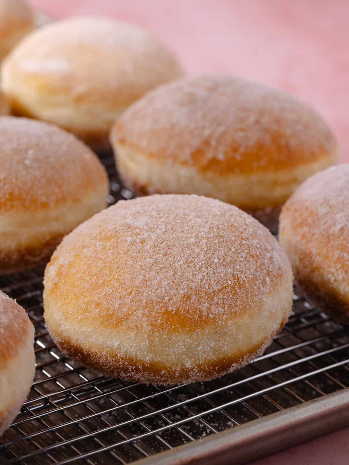 Donuts coated in sugar is sitting on a wire rack.