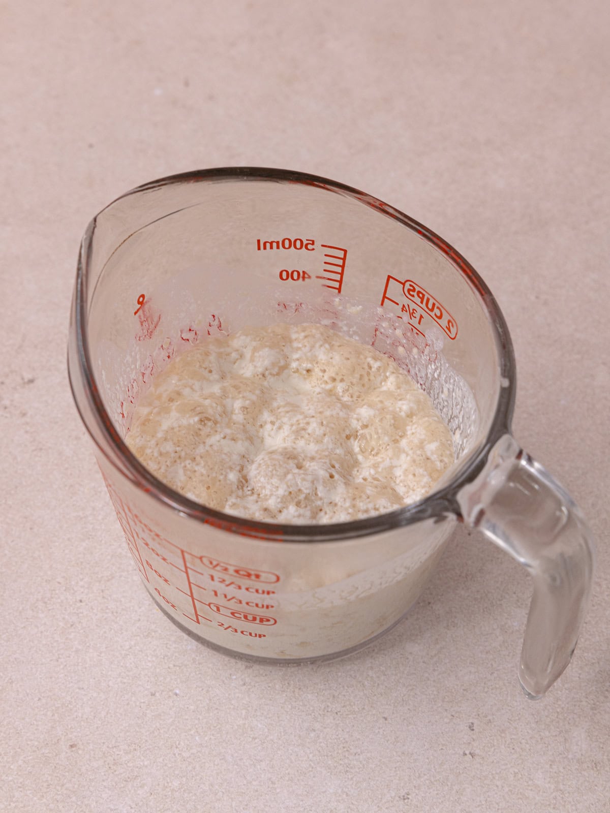 A large measuring cup with dloomed yeast in buttermilk