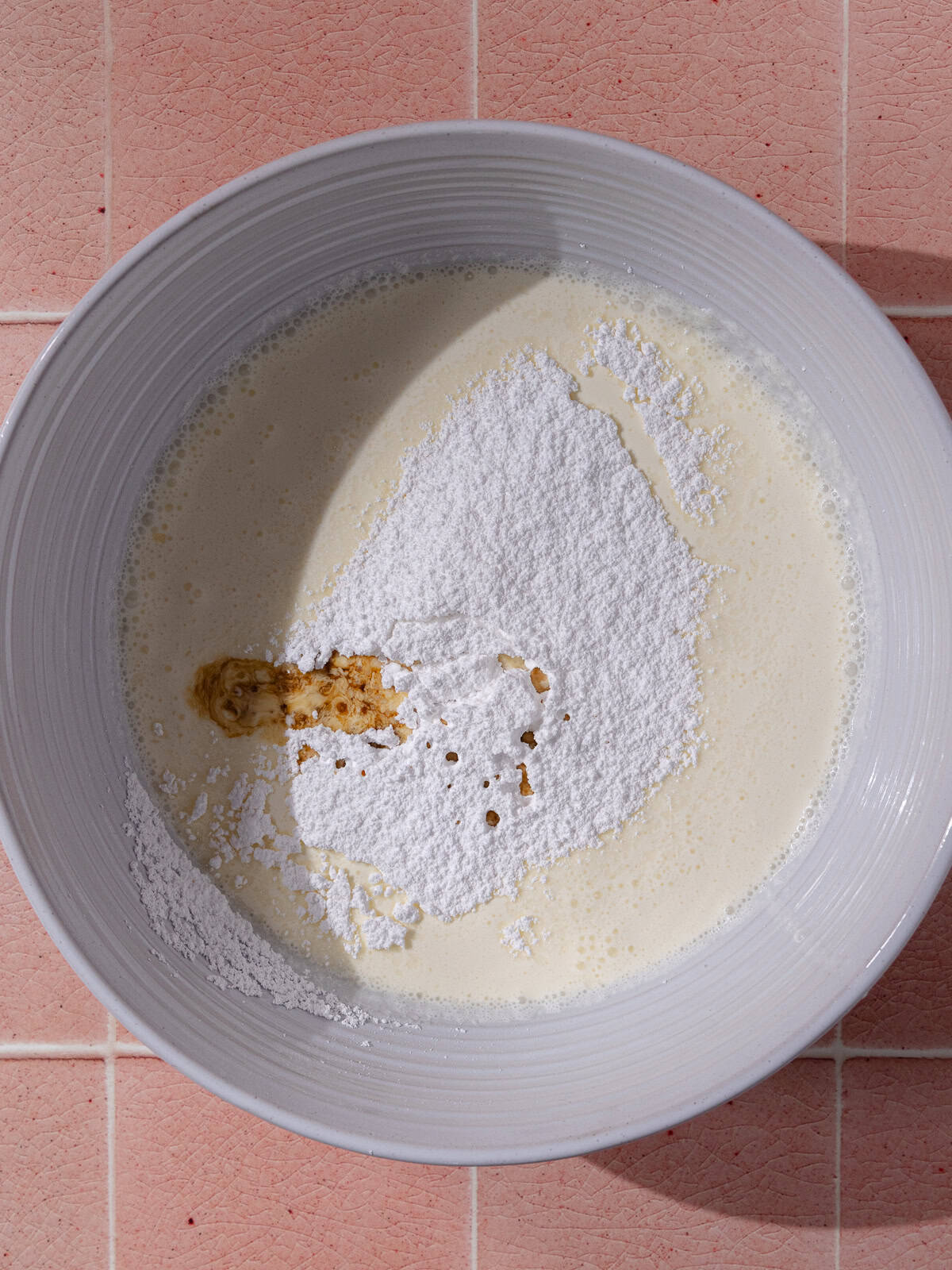 Heavy cream, powdered sugar and vanilla extract are in a large white mixing bowl.