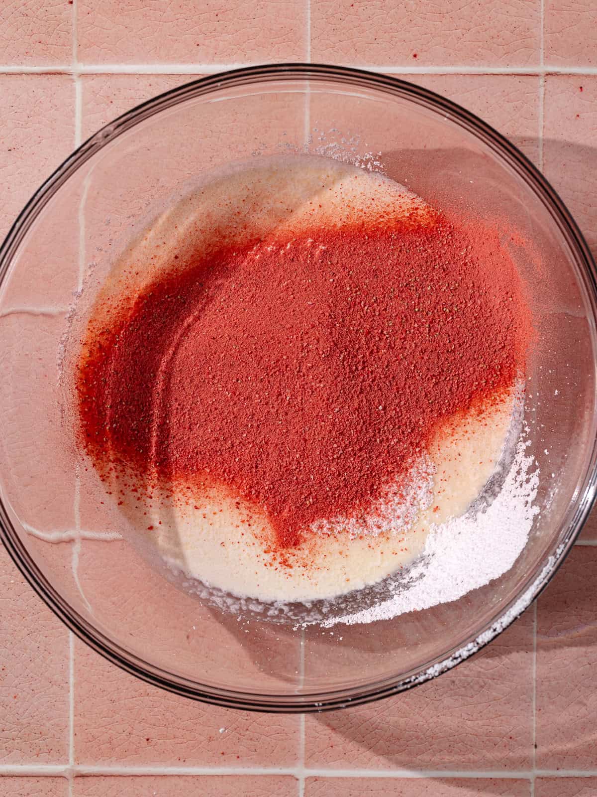 Whipped cream, powdered sugar and freeze-dried strawberry powder in a large glass mixing bowl.