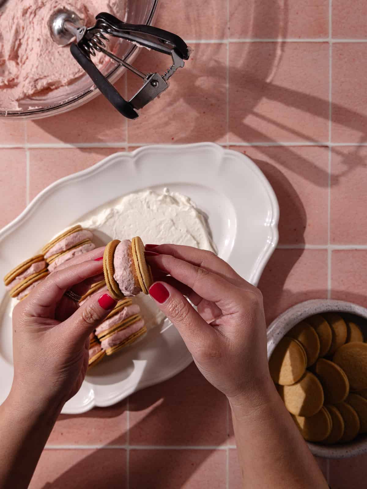 Strawberry whipped cream is spread in between cookies.