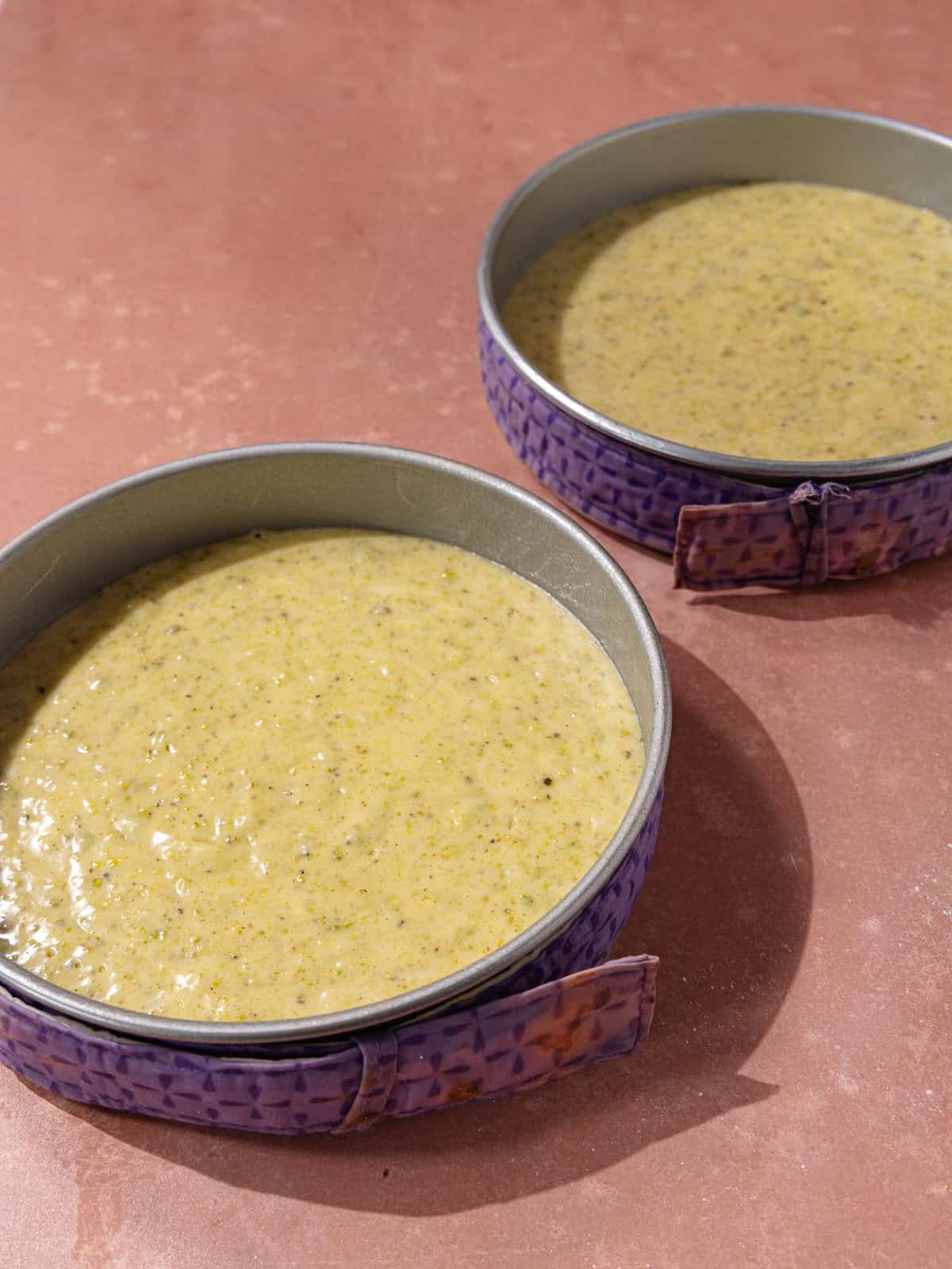 Cake pans are filled with cake batter and wrapped with cake strips.