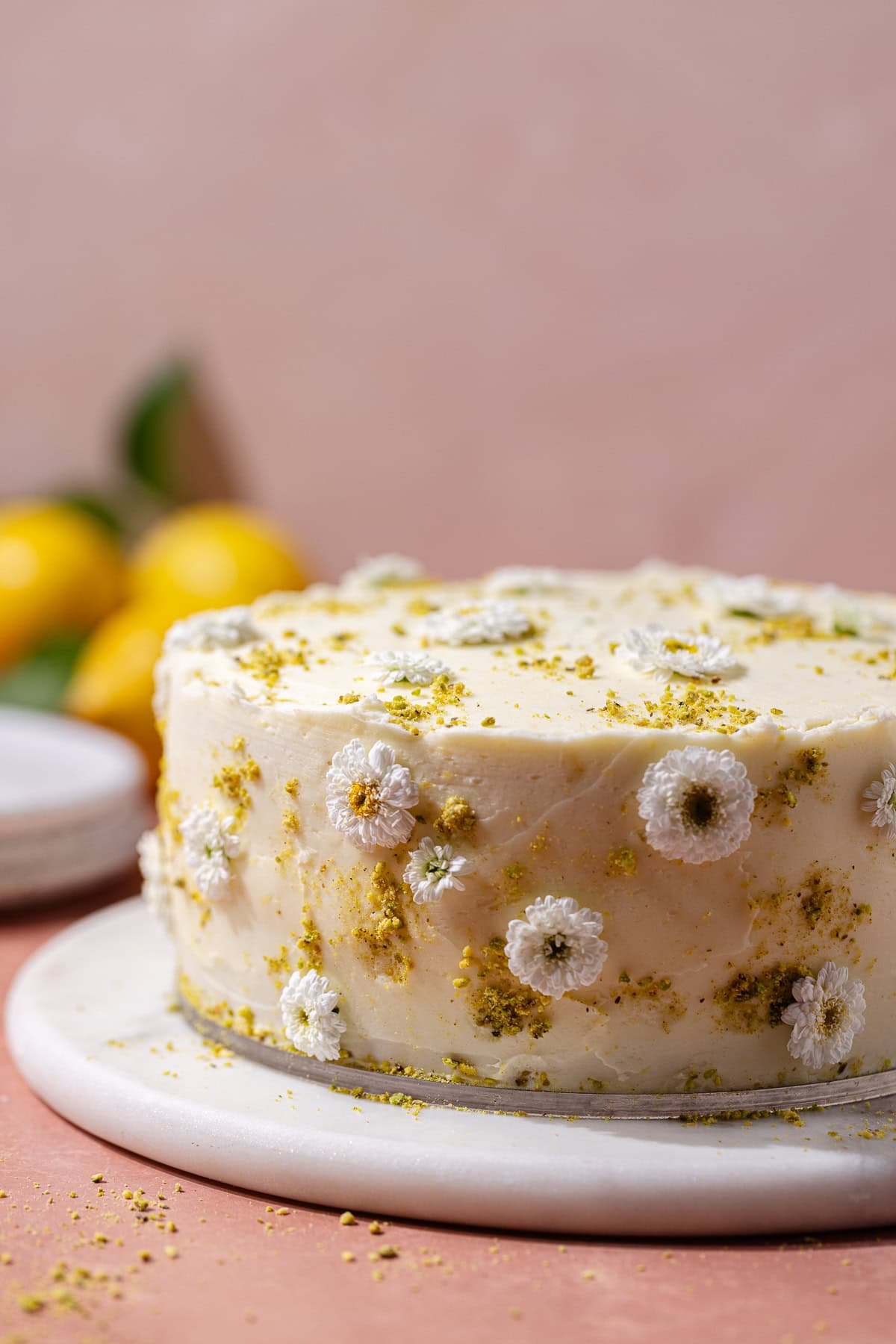 Pistachio lemon cake decorated with little flowers and ground pistachios on a serving plate.