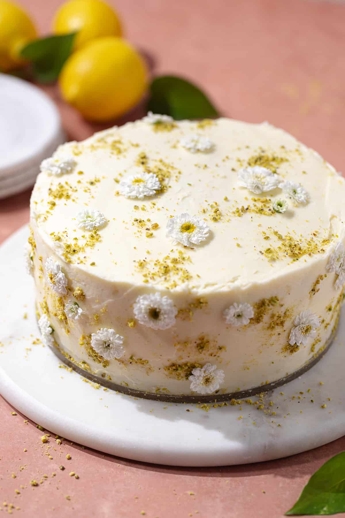 Pistachio lemon cake decorated with little flowers and ground pistachios on a serving plate.