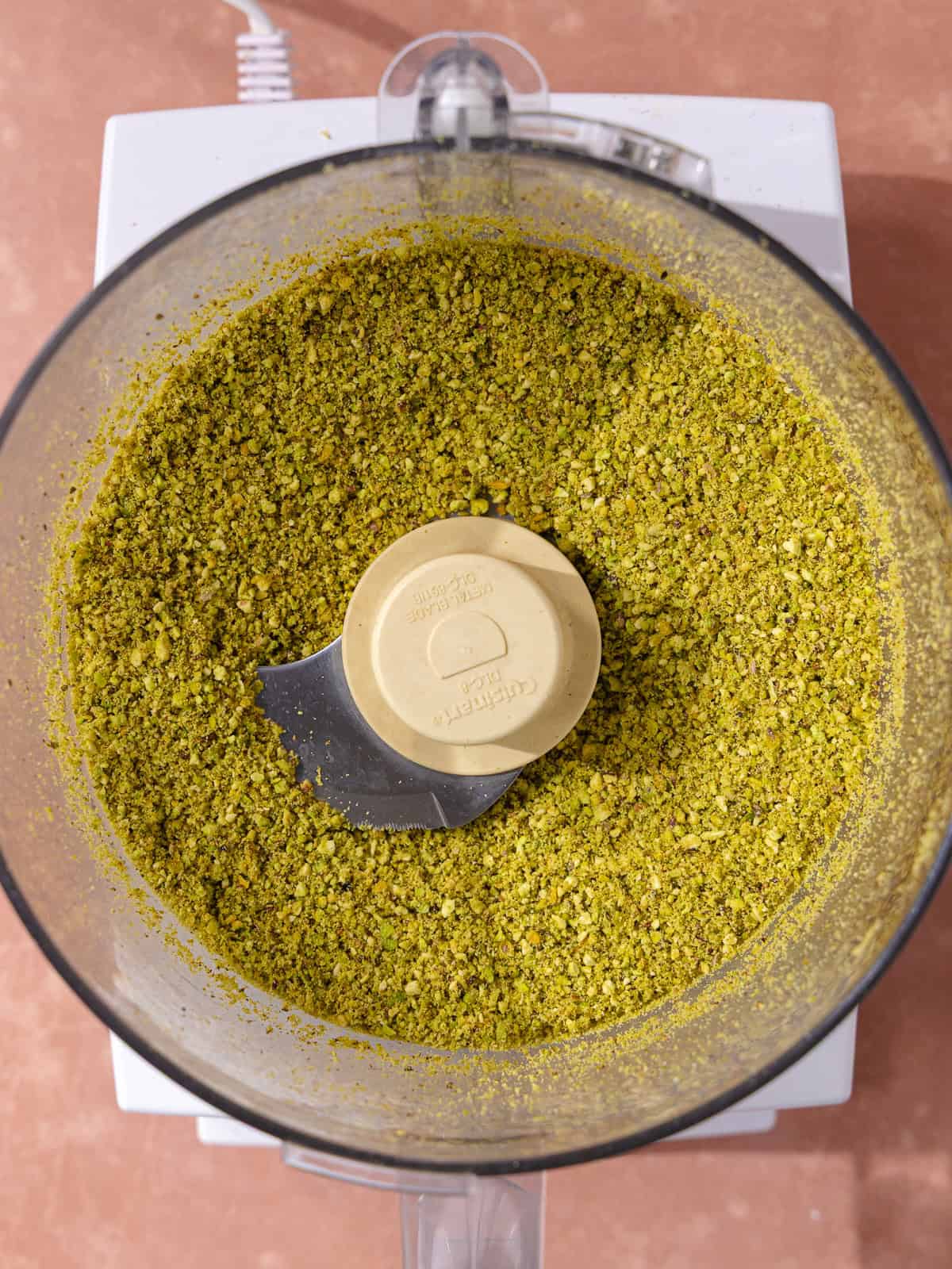 Raw pistachios are finely ground in a food processor.