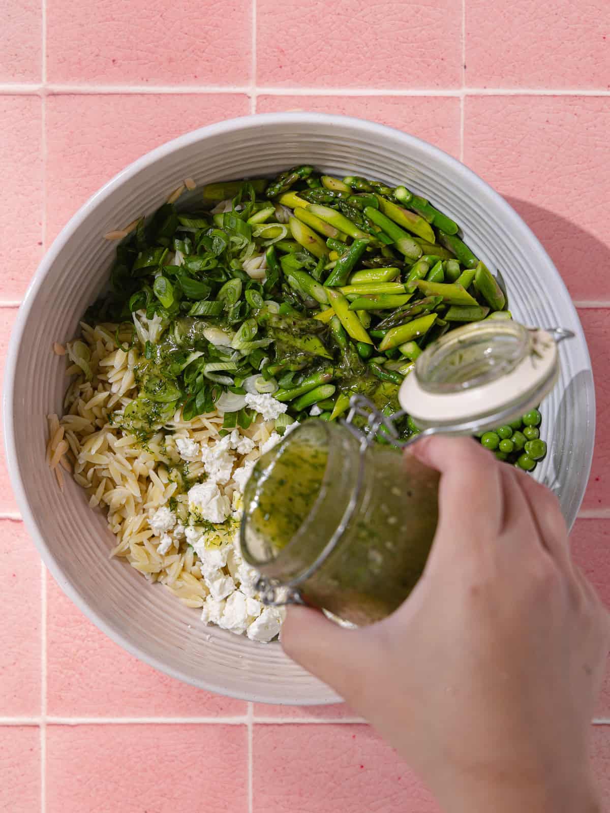 Lemon dill dressing is poured over spring orzo pasta salad.